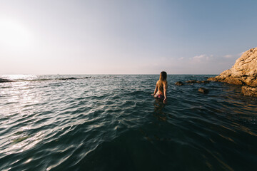 Girl with long hair swims in the sea, splashes water on a background of a sunset sky