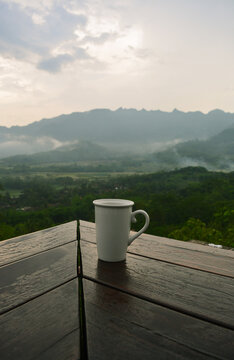 A cup of warm chocolate on a wooden table with a natural view of the Manoreh mountains in Magelang, Central Java - Indonesia