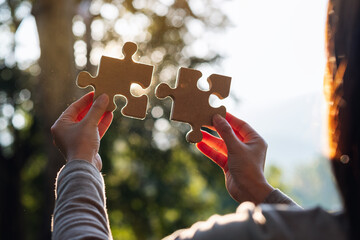 Closeup image of a woman holding and putting a piece of wooden jigsaw puzzle together in the...