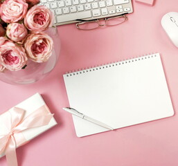 women's office desk, workspace top view on pink background with laptop, beautiful pink roses flowers, gift box, accessories, notebook mock up, glasses. Copy space. Flat lay. Holiday, birthday concept