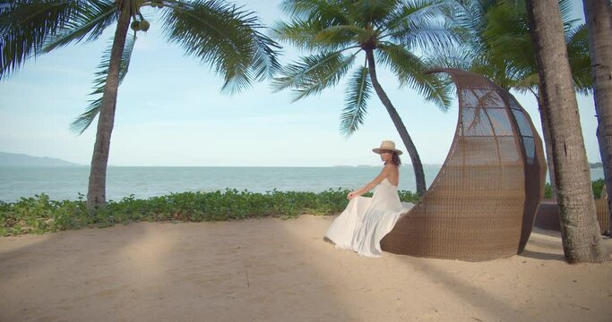 Woman seats on the beach loge against the ocean, camera moves to her
