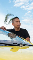 Latino man next to his yellow taxi car, wearing a black shirt during the cloudy day.