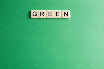 the words green written as a flat lay in wood scrabble tiles on a plain green background