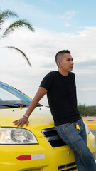 hispanic man next to his yellow taxi car, wearing a black shirt during the cloudy day.