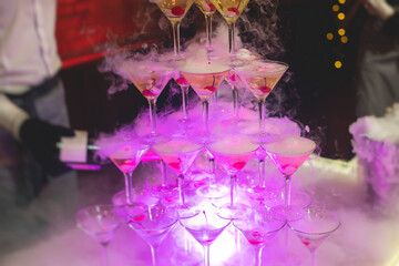 Glasses with alcoholic beverages in the pyramid, filling and pouring beautiful pyramid line of different colored alcohol cocktails with champagne on a party, catering banquet table