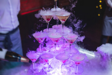 Glasses with alcoholic beverages in the pyramid, filling and pouring beautiful pyramid line of different colored alcohol cocktails with champagne on a party, catering banquet table