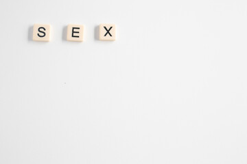 the word sex written as a flat lay in wood scrabble tiles on a plain white background