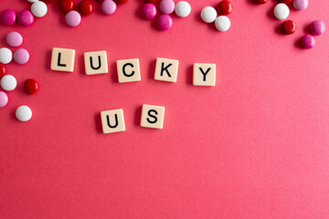 the words lucky you written as a flat lay in wood scrabble tiles on a plain red background surrounded by red, white, and pink candies