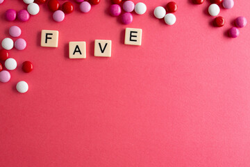the word fave written as a flat lay in wood scrabble tiles on a plain red background surrounded by red, white, and pink candies