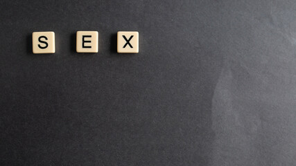 the words sex written as a flat lay in wood scrabble tiles on a plain black background - Powered by Adobe