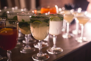 View of alcohol setting on catering banquet table, row line of different colored alcohol cocktails on a party, martini, vodka, spritz and others on decorated catering table event