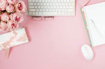 Female workspace with laptop, pink roses flowers in a vase, gift box, accessories top view on pink background with copy space. Holiday, birthday concept.
