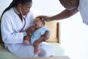 African pediatrician holding and using stethoscope to listen to baby and checking heart beat, father touches the head to comfort the baby as the pediatrician examines the 5-month-old baby crying