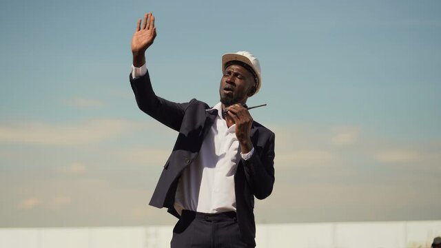 african american architect in suit and hard hat talking by walkie talkie control and communication with worker outdoors on construction site. contractor using radio operation in industry