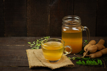 Tamarind juice in glass and tamarind fresh tropical fruit with leaf on wooden background.