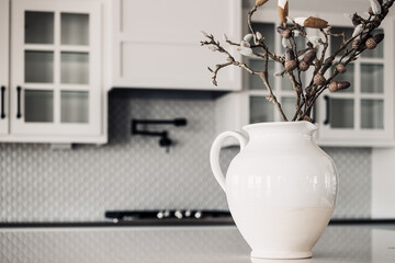 White modern vase on sitting on a white marble counter top in a modern kitchen with white cabinets and white back splash  