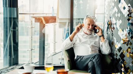 Elderly grey-haired businessman in white shirts are happily calling because they receive retirement insurance or listening to post-retirement insurance offers in a modern business lounge high up tower