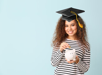 African-American girl in graduation hat and with piggy bank on color background. Concept of savings...