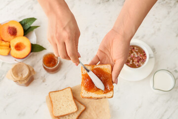 Obraz na płótnie Canvas Woman spreading tasty peach jam onto slice of bread on light background