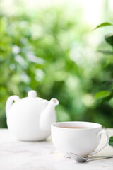 Teapot and cup of tea on table against blurred background