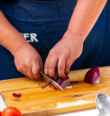 manos con cuchillo  cortando cebolla morada en tabla de madera 