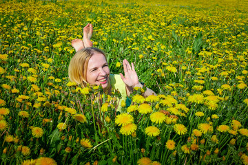 Beautiful young woman on a field with green grass and yellow dandelion flowers in a sunny day. Girl on nature with yellow flowers