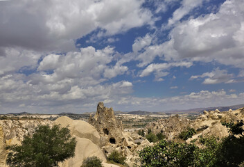 Fototapeta na wymiar The amazing landscape of Cappadocia. In the foreground are rocks with caves. Silhouettes of mountains in the distance. Blue sky with scenic cumulus clouds. Turkey.