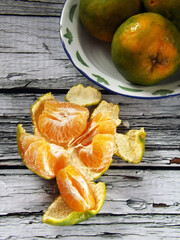 Image of the whole and peeled of jeruk keprok or Indonesian local orange fruits which commonly has green with bit yellow skin. The taste is very refreshing, sweet with bit sour. High angle picture.