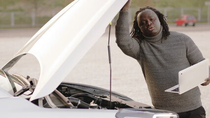 Mobile car assistance. African american black man running diagnostic on broken car on his laptop. High quality photo