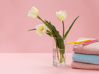 Bouquet of yellow tulips in vase with towels on a pink background.