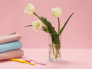 Bouquet of yellow tulips in vase with towels on a pink background.