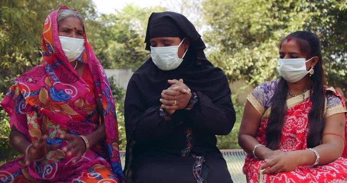Handheld slow-motion shot of 3 women wearing face masks with Sari and Hijab discuss worried apprehensive discomfort new normal future indecision what the hell during coronavirus covid-19 