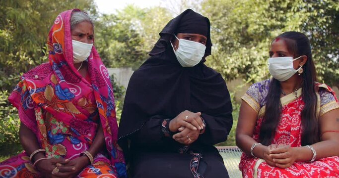 Handheld slow-motion shot of 3 women wearing face masks with Sari and Hijab discuss worried apprehensive discomfort new normal future indecision what the hell during coronavirus covid-19 