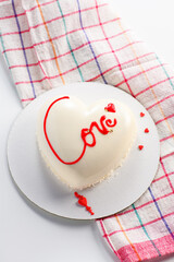 A cake in heart shape.  Mousse light cake in the shape of a heart with the inscription love on a checkered towel. Valentine's Day. Vertical photo