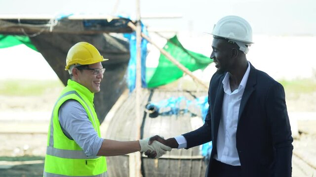 asian foreman and african american architect handshake  outdoors on construction site at village . contractor worker Inspection with builder . Engineer and foreman . quality control