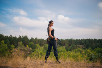 Girl with a pistol in nature. Against the background of yellow grass. The female army on the hunt.