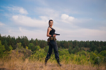 Girl with a pistol in nature. Against the background of yellow grass. The female army on the hunt.