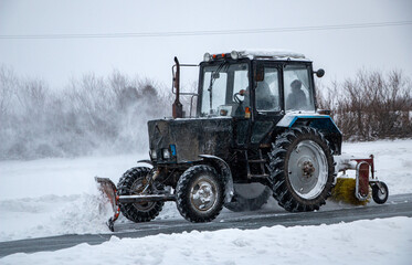 an old snow-covered tractor with  blade removes snow from the road, sweeps snow from the road with ...