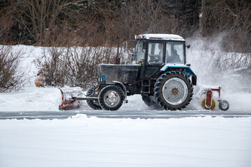 an old snow-covered tractor with  blade removes snow from the road, sweeps snow from the road with ...