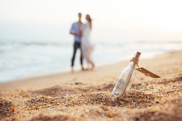 couple walking on the beach . couple on the beach . 
bottle in the sand