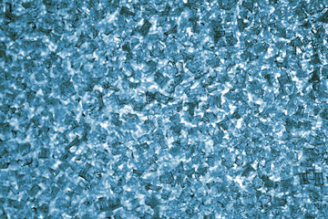 Ice and frost crystals on the window pane close-up. Blue tinted wallpaper. Unusual festive background for winter, Christmas or New Year. Backdrop looks like a bunch of broken glass fragments. Macro
