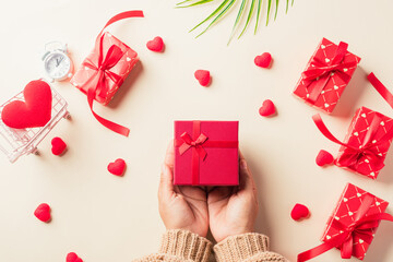 Valentine's day and birthday. Woman hands holding gift or present box decorated and red heart surprise on cream pastel background, Female's hand hold gift box package in craft paper Top view flat lay