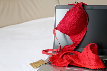 Female lace panties, red bra and condom on laptop on a bed. Concept of sex after work, contraception, seductive lingerie