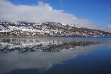 mirror reflection of the mountains and clouds in Serre Ponçon lake, France on a cold winter day