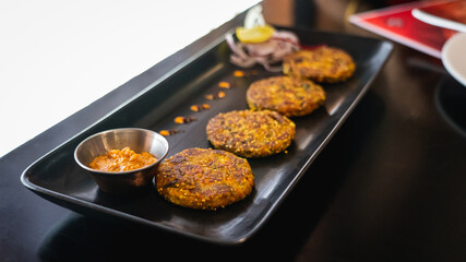 Selective focus of potato quinoa patties served with red pepper dip on a black serving tray.