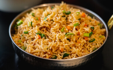 A close up of Vegetable Fried Rice served in a wok pan on a black background.