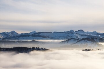 Obraz na płótnie Canvas Winterlandschaft der schneebedeckten bayerischen Alpen über Wolken vor blauem Himmel