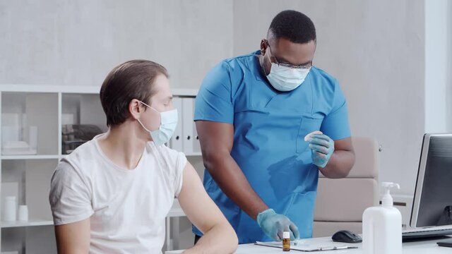 African-American doctor makes a coronavirus vaccine using a syringe and hypodermic needle. Medical worker and patient at the hospital office. Vaccination and safety concept.