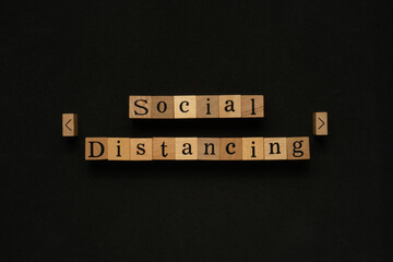 Flat lay view of the social distancing word on wooden block. Creative concept with black background.