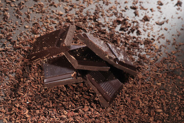 Broken dark chocolate bar and chocolate flakes on black kitchen table